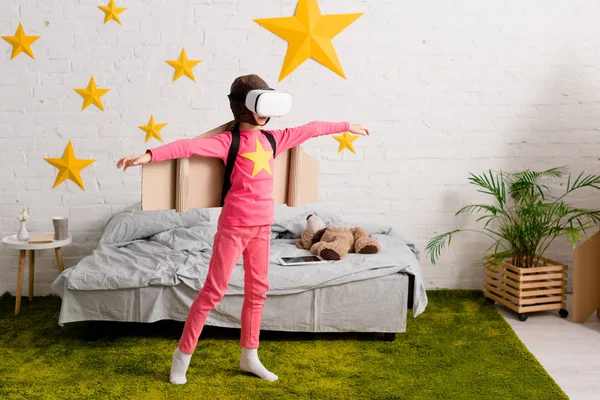 Vista completa de niño despreocupado en auriculares vr agitando las manos en el dormitorio - foto de stock