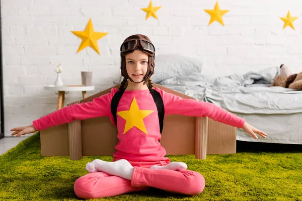 Inspired kid in flight helmet sitting in lotus pose on carpet — Stock Photo