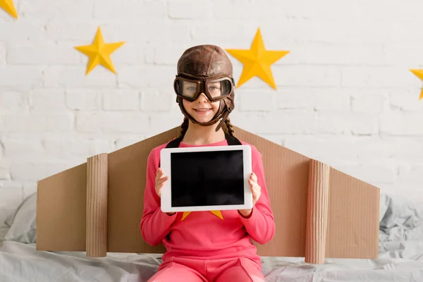 Smiling kid with cardboard wings holding digital tablet with blank screen — Stock Photo