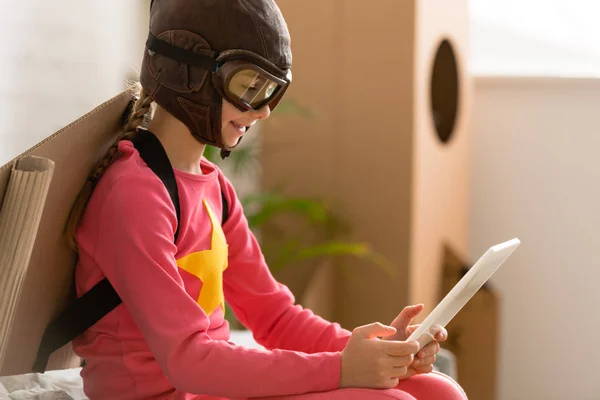 Smiling kid in flight helmet using digital tablet at home — Stock Photo