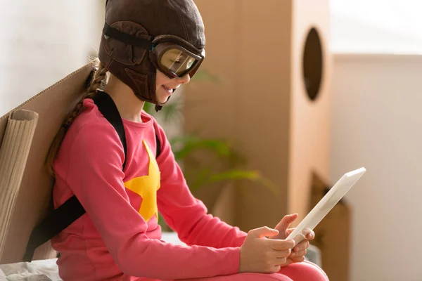 Criança sorridente no capacete de voo usando tablet digital em casa — Fotografia de Stock