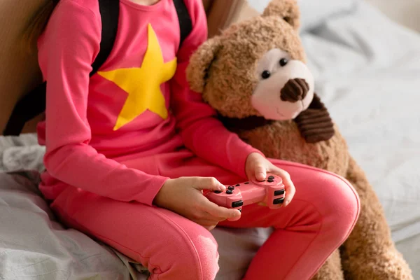 Partial view of kid with teddy bear holding gamepad — Stock Photo