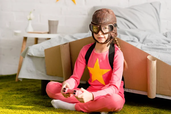 Enfant dans le casque de vol assis sur le tapis avec une manette de jeu — Photo de stock