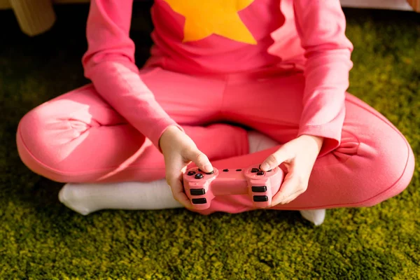 Partial view of kid sitting on green carpet with joystick — Stock Photo