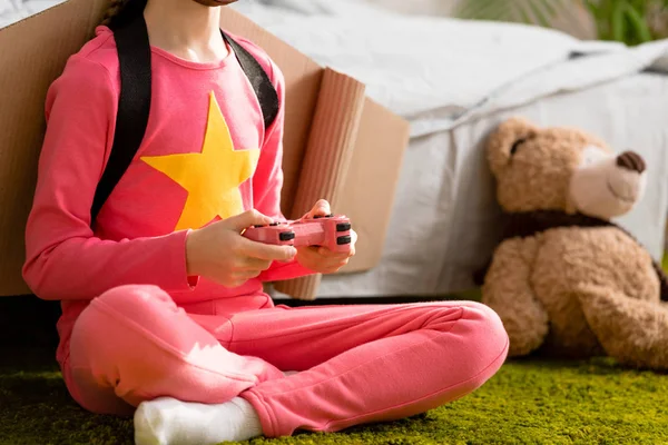 Vista parcial del niño en ropa rosa sentado en la alfombra con joystick - foto de stock