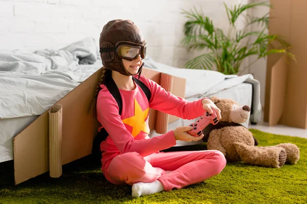 Enfant souriant avec manette assise sur le tapis dans la chambre — Photo de stock