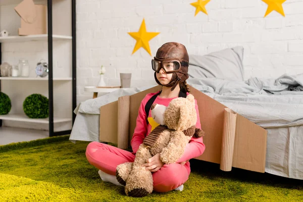 Serious kid with teddy bear sitting on carpet in bedroom — Stock Photo