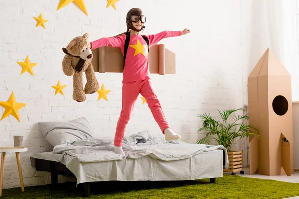 Funny kid with teddy bear jumping on bed — Stock Photo