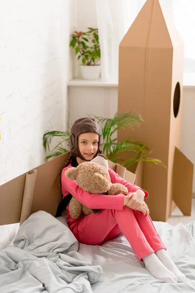 Riendo niño con oso de peluche sentado en la cama - foto de stock