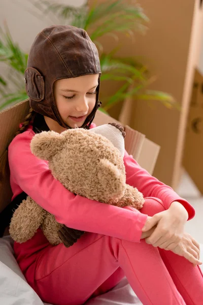 Kid in pink clothes and flight helmet holding teddy bear — Stock Photo