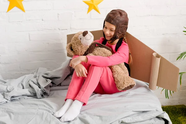 Усміхнена дитина з плюшевим ведмедем сидить на ліжку — стокове фото