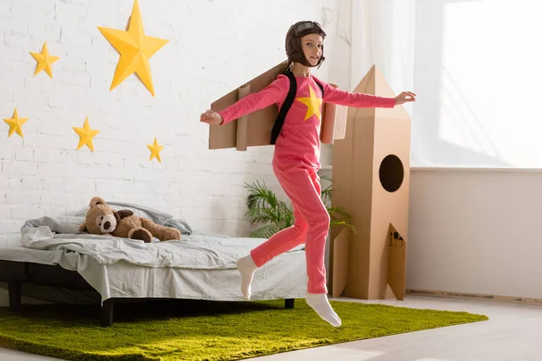 Enfant inspiré avec des ailes en carton sautant dans la chambre avec le sourire — Photo de stock