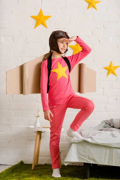 Cheerful child with cardboard wings looking away — Stock Photo