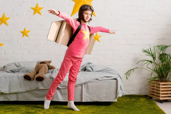 Glückliches Kind mit Pappflügeln hat Spaß im Schlafzimmer — Stockfoto