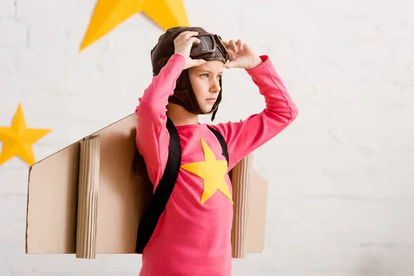 Confident child with cardboard wings touching goggles — Stock Photo
