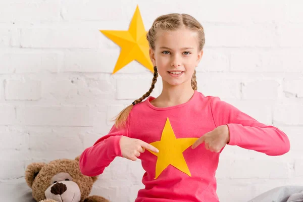 Веселый ребенок с косичками, указывающими пальцами на желтую звезду — стоковое фото