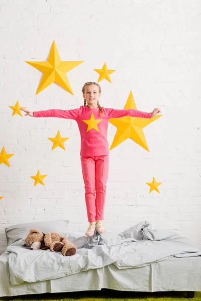 Criança excitada em roupas rosa pulando na cama — Fotografia de Stock