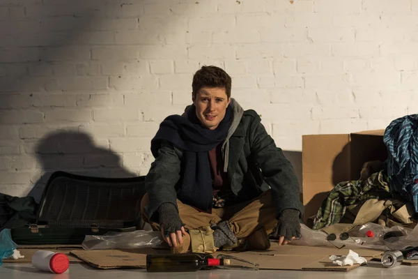 Obdachloser sitzt auf Pappe, umgeben von Müllhalde — Stockfoto