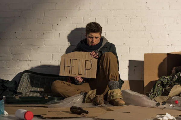 Homeless depressed man sitting on cardboard holding card with 