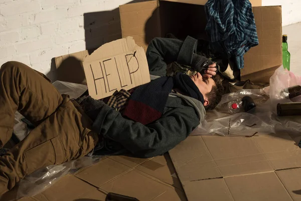 Homeless man lying on cardboard on rubbish dump and holding card with 