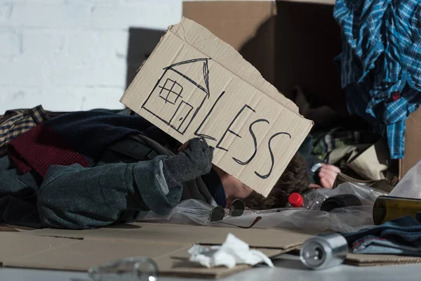 Homeless man lying on rubbish damp with symbol of house and 