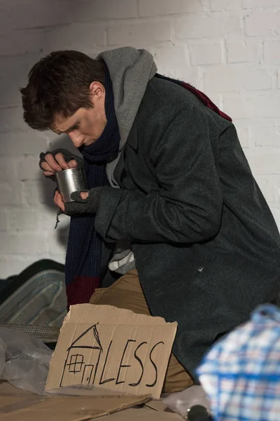 Бездомний жебрак дивиться в бляшанку, сидячи на сміттєвому звалищі — стокове фото