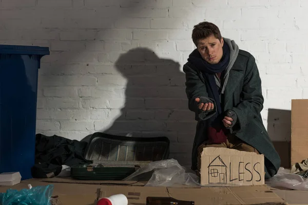 Homeless beggar man sitting on rubbish dump by white brick wall — Stock Photo