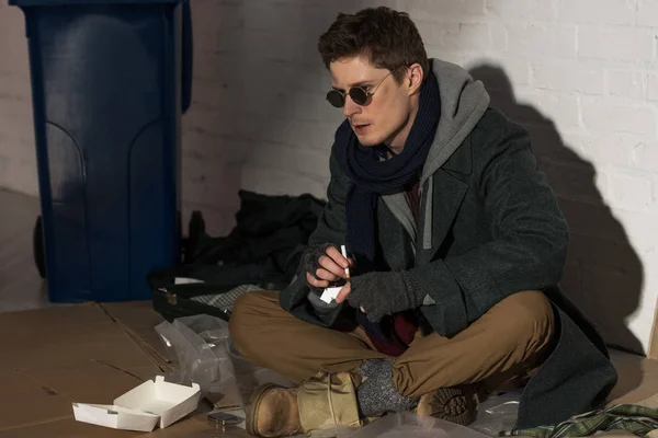 Homeless man sitting on rubbish damp and holding cigarette — Stock Photo