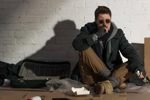 Безпритульний чоловік курить сигарету, сидячи на сміттєвому звалищі — стокове фото