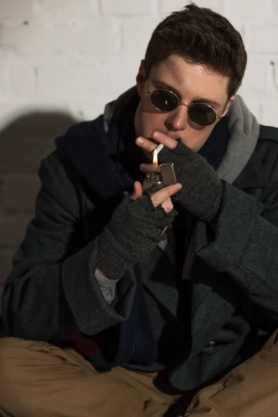 Hombre sin hogar en guantes sin dedos iluminación cigarrillo - foto de stock