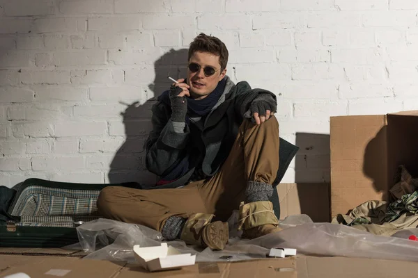 Vagabundo sentado en el basurero y fumando cigarrillo - foto de stock