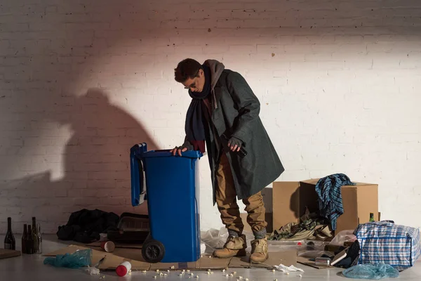 Бездомний чоловік у темному одязі рветься в контейнері для сміття — стокове фото