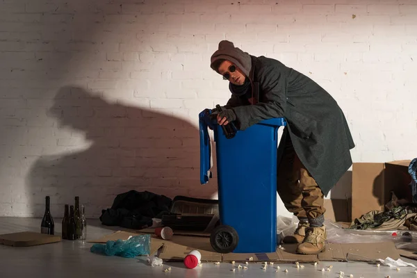 Бездомный в темной одежде рылся в мусорном контейнере — стоковое фото
