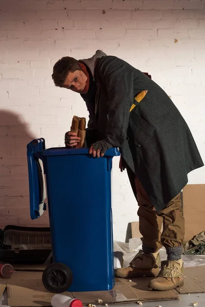 Hungry homeless man getting bread baguette from garbage container — Stock Photo