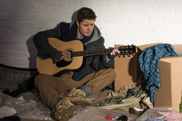 Бездомний чоловік грає на гітарі, сидячи на сміттєвому звалищі — стокове фото