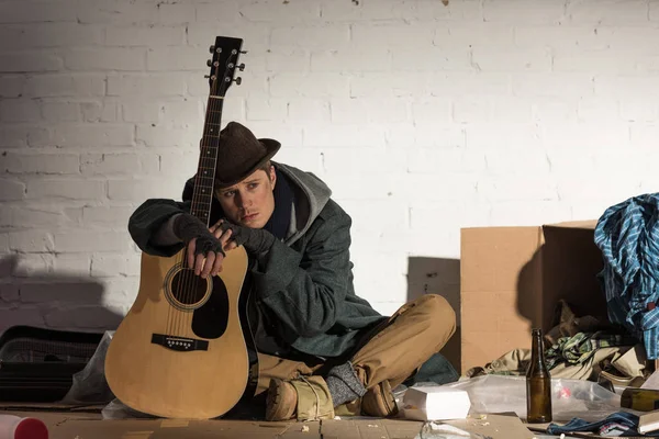 Depressed homeless man leaning on guitar while sitting on street rubbish dump — Stock Photo