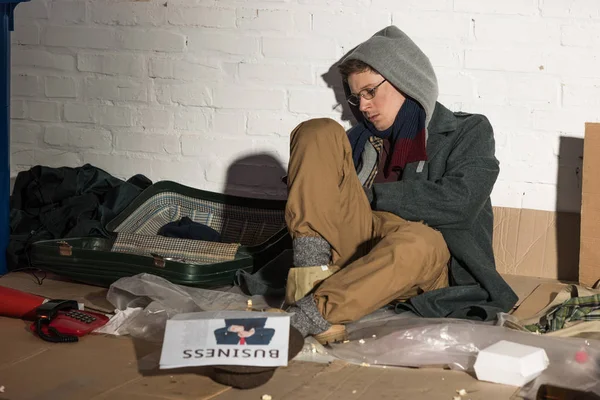 Бездомный сидит на помойке с деловой газетой — стоковое фото