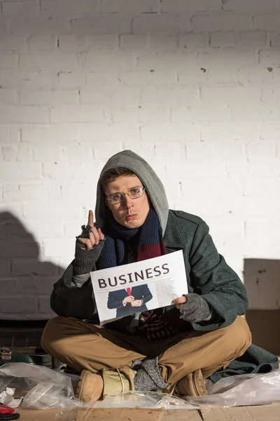 Удивленный бездомный держит деловую газету и показывает знак идеи — стоковое фото
