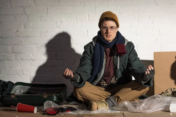 Homeless man sitting in lotus pose near white brick wall on rubbish dump — Stock Photo