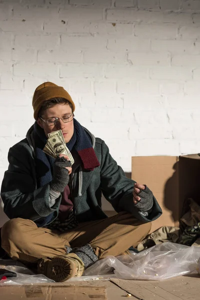 Homeless man sitting on rubbish dump and holding money — Stock Photo