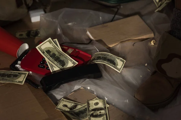 Cropped view of male leg in boot near vintage phone, book and money scattered on floor — Stock Photo