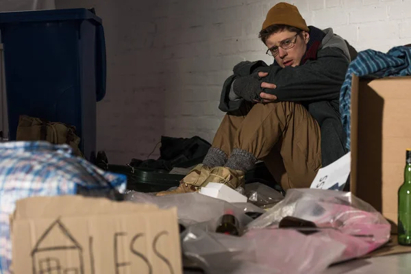 Enfoque selectivo de depresiones hombre sin hogar sentado por la pared de ladrillo en basurero - foto de stock