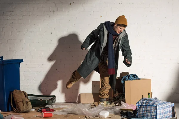 Hombre sin hogar enojado pateando caja de cartón con basura - foto de stock