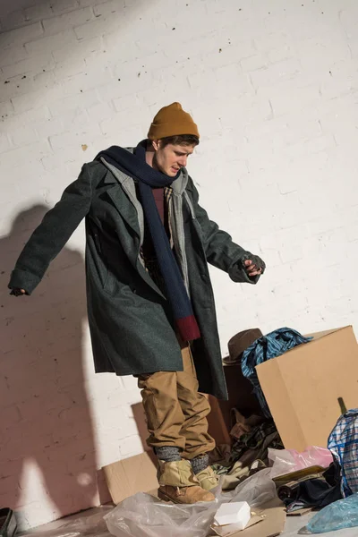 Arrabbiato senzatetto in piedi sopra scatola di cartone con immondizia — Foto stock