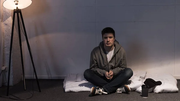 Homme assis sur un matelas blanc disposé sur le sol dans la chambre noire — Photo de stock