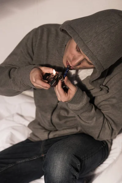 Selective focus of addicted man lightening smoking pipe with metallic lighter — Stock Photo