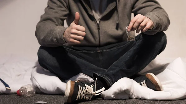 Suchtkranker Mann hält Packung Marihuana in der Hand und zeigt Daumen hoch — Stockfoto