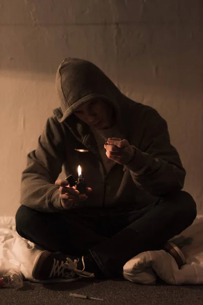 Junkie-Mann sitzt im dunklen Raum und erhitzt Kochlöffel mit Heroin auf Feuerzeug — Stockfoto