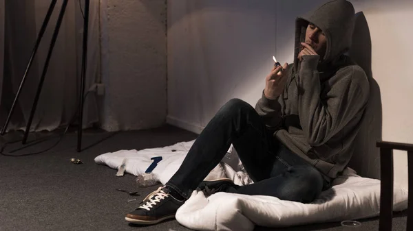 Junkie man smoking marijuana rolled cigarette white sitting on mattress on floor — Stock Photo