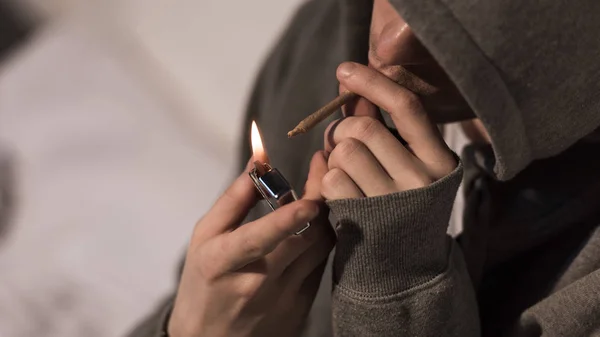 Selective focus of junkie man lightening rolled marijuana cigarette — Stock Photo